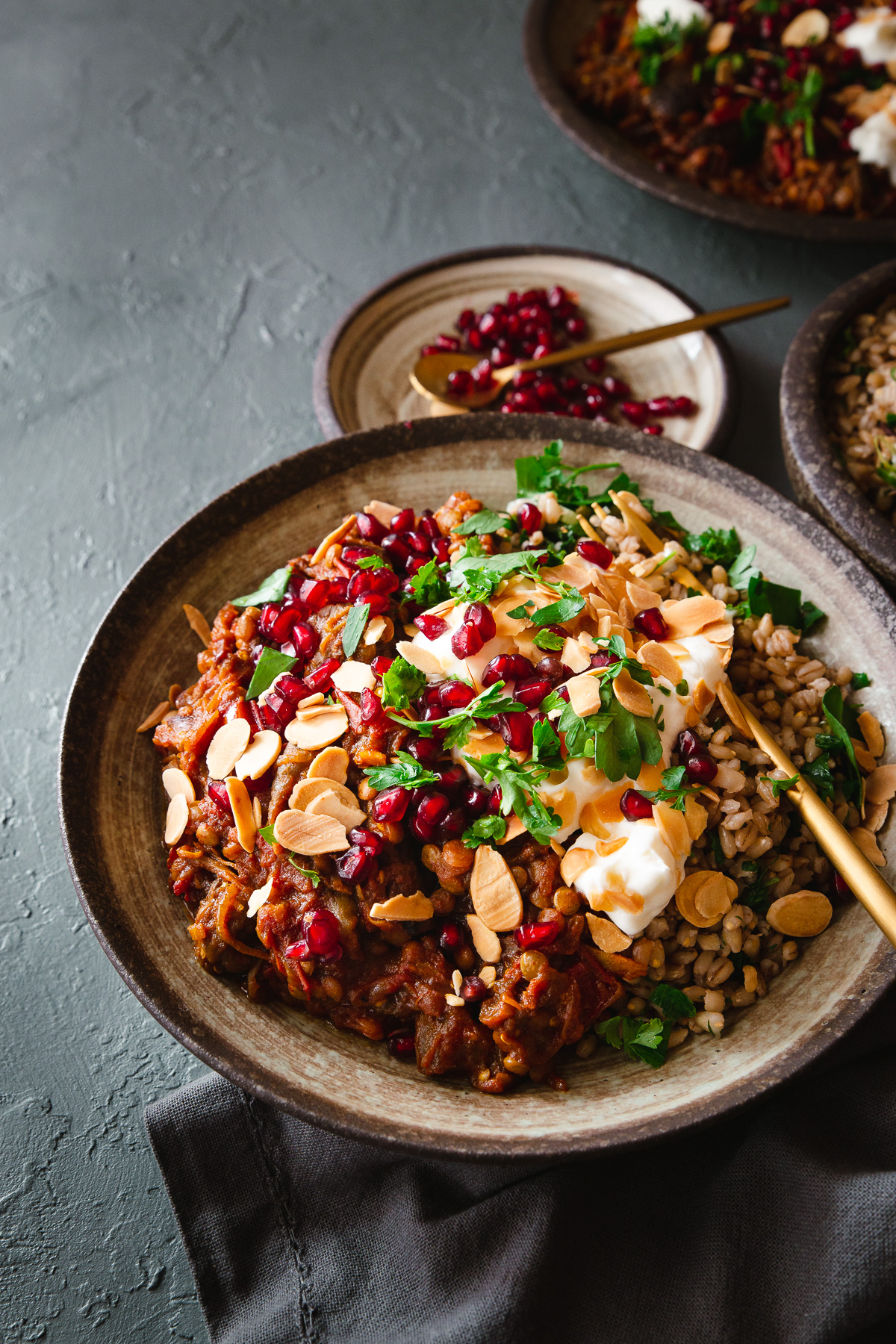 A bowl of barley topped with Persian aubergine and black lime stew and toppings.