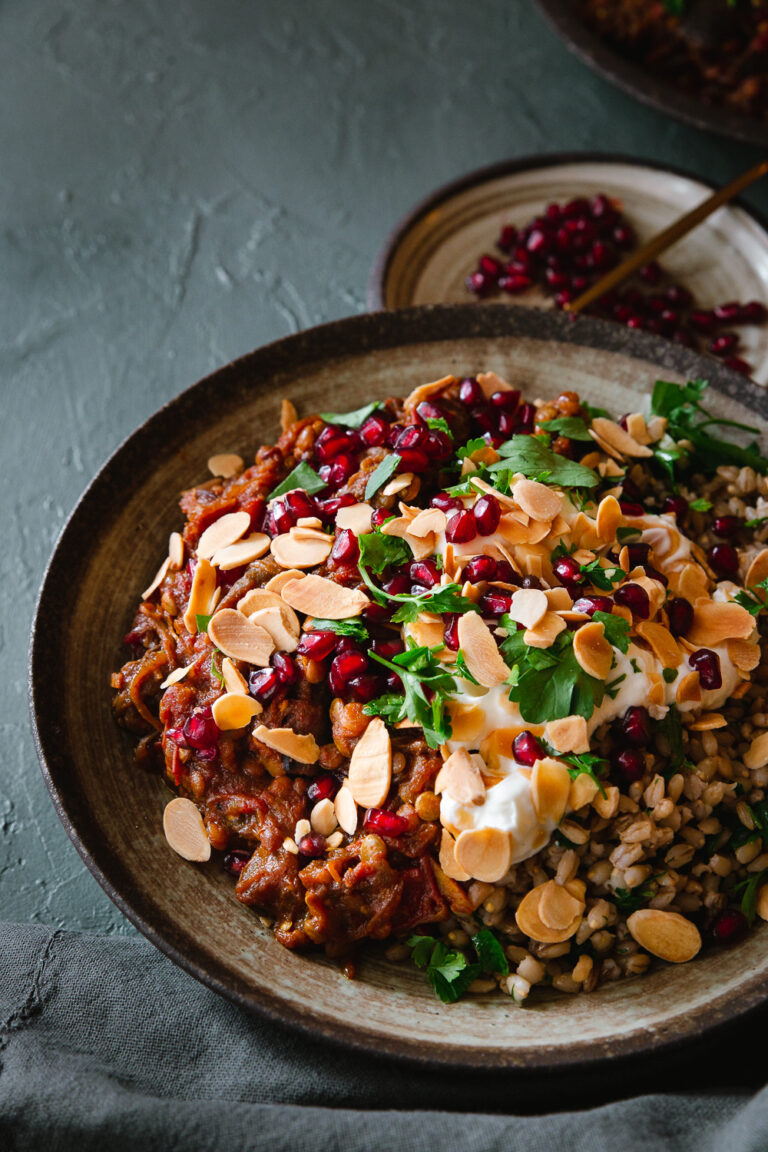 A bowl of Persian aubergine stew with yoghurt, almonds, pomegranate and coriander.