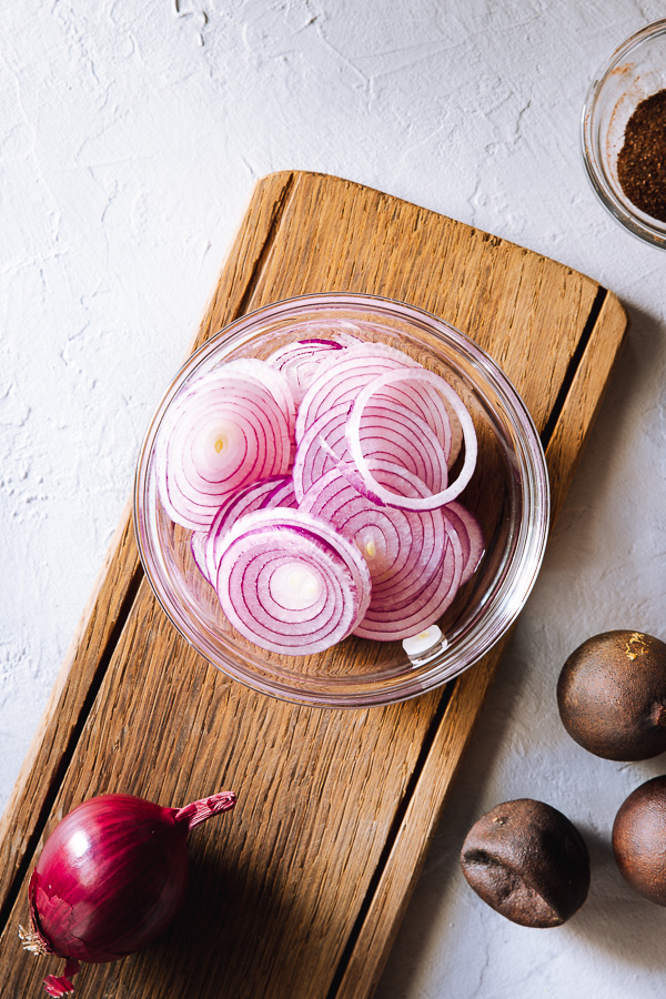 Sliced red onions in a glass bowl on a wooden serving board.