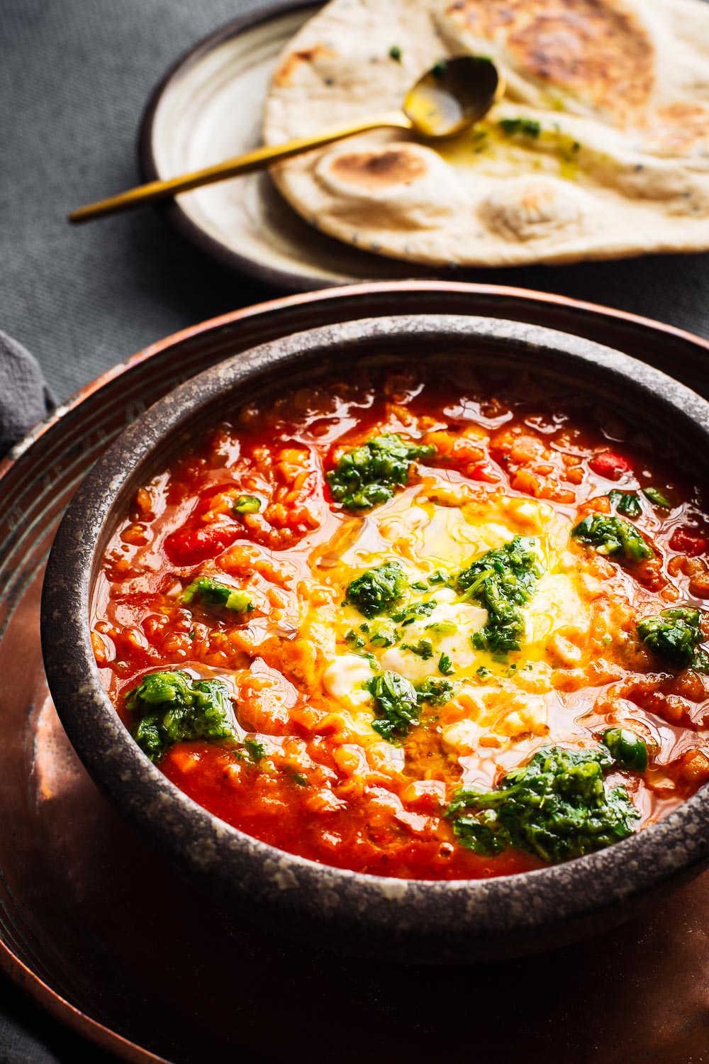 Close-up of a bowl of red lentil soup with a flatbread in the background.