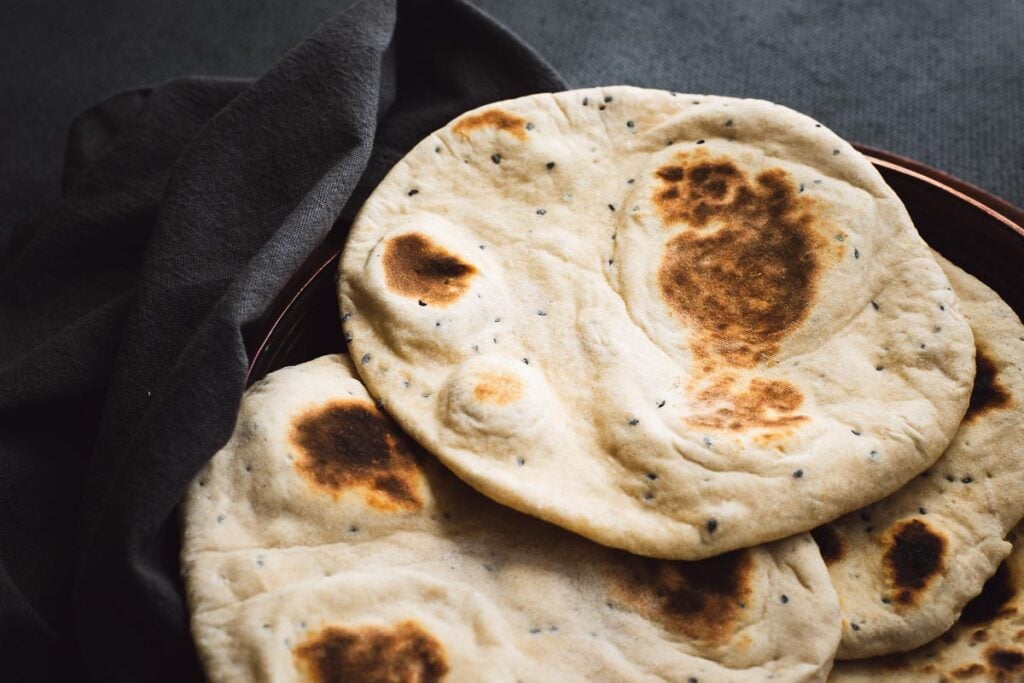 Yoghurt flatbreads in a copper bowl on a dark grey background.