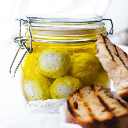 Close-up of labneh balls in olive oil in a sealed glass jar.
