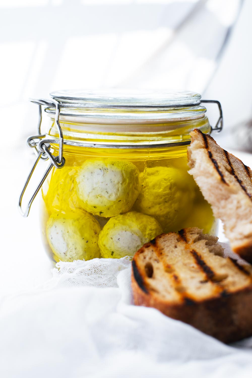 Close-up of labneh balls in olive oil in a sealed glass jar.