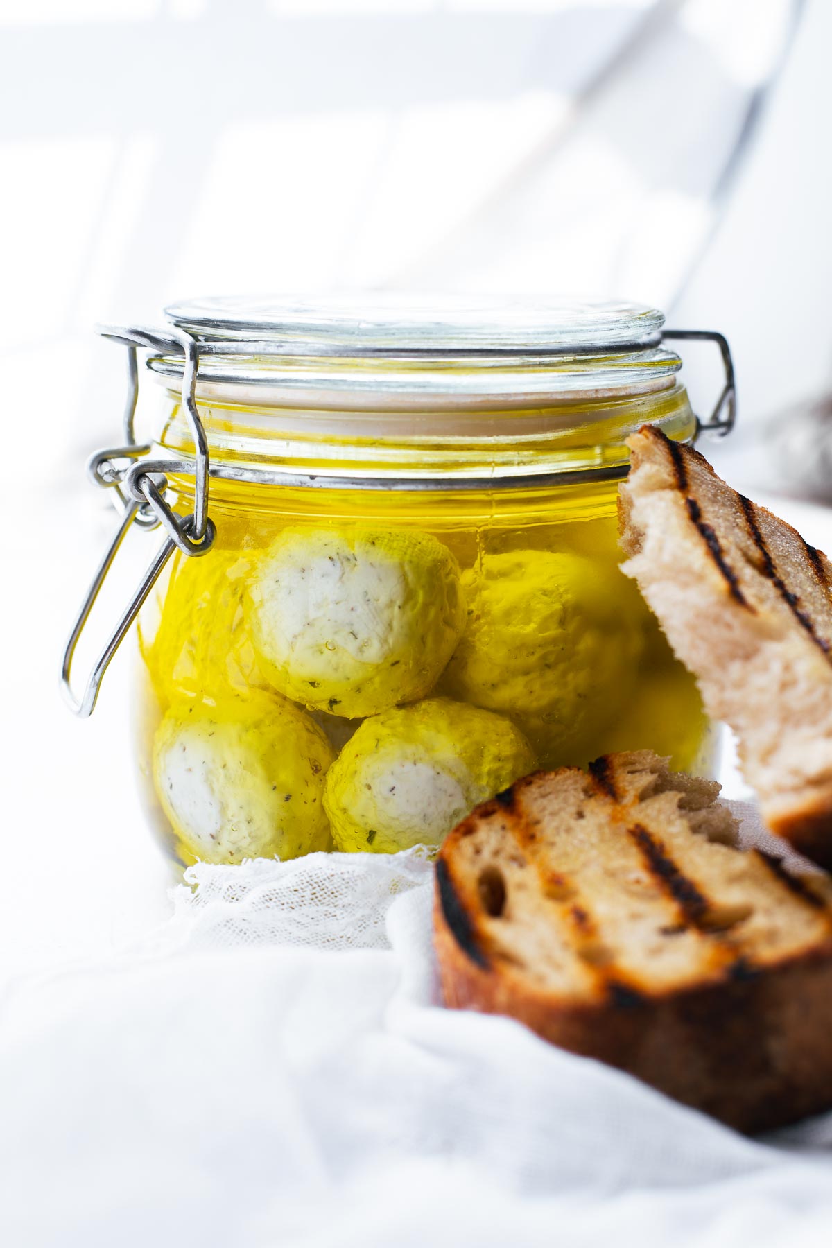 Garlic and herb labneh balls in olive oil, stored in a glass jar and served with toasted sourdough.
