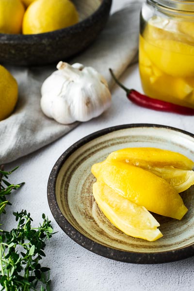 A preserved lemon on a plate surrounded with garlic, chilli and thyme.