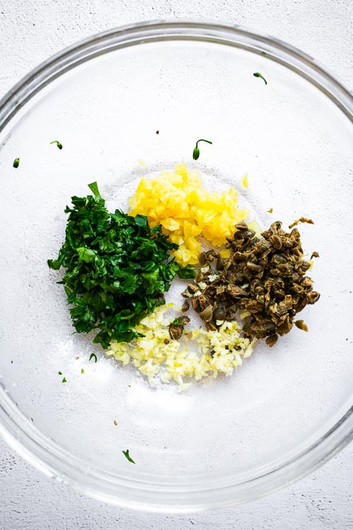 Chopped ingredients for a preserved lemon marinade in a glass bowl.