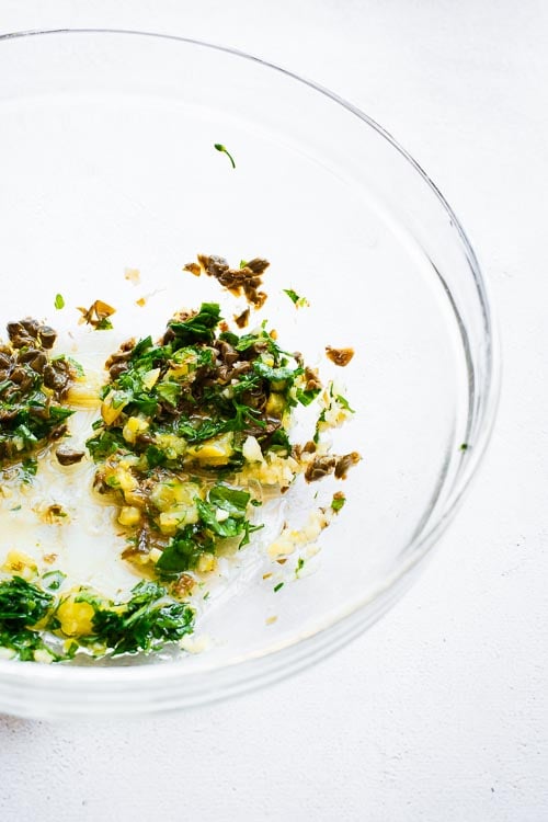 Ingredients for the preserved lemon and caper marinade mixed in a glass bowl.