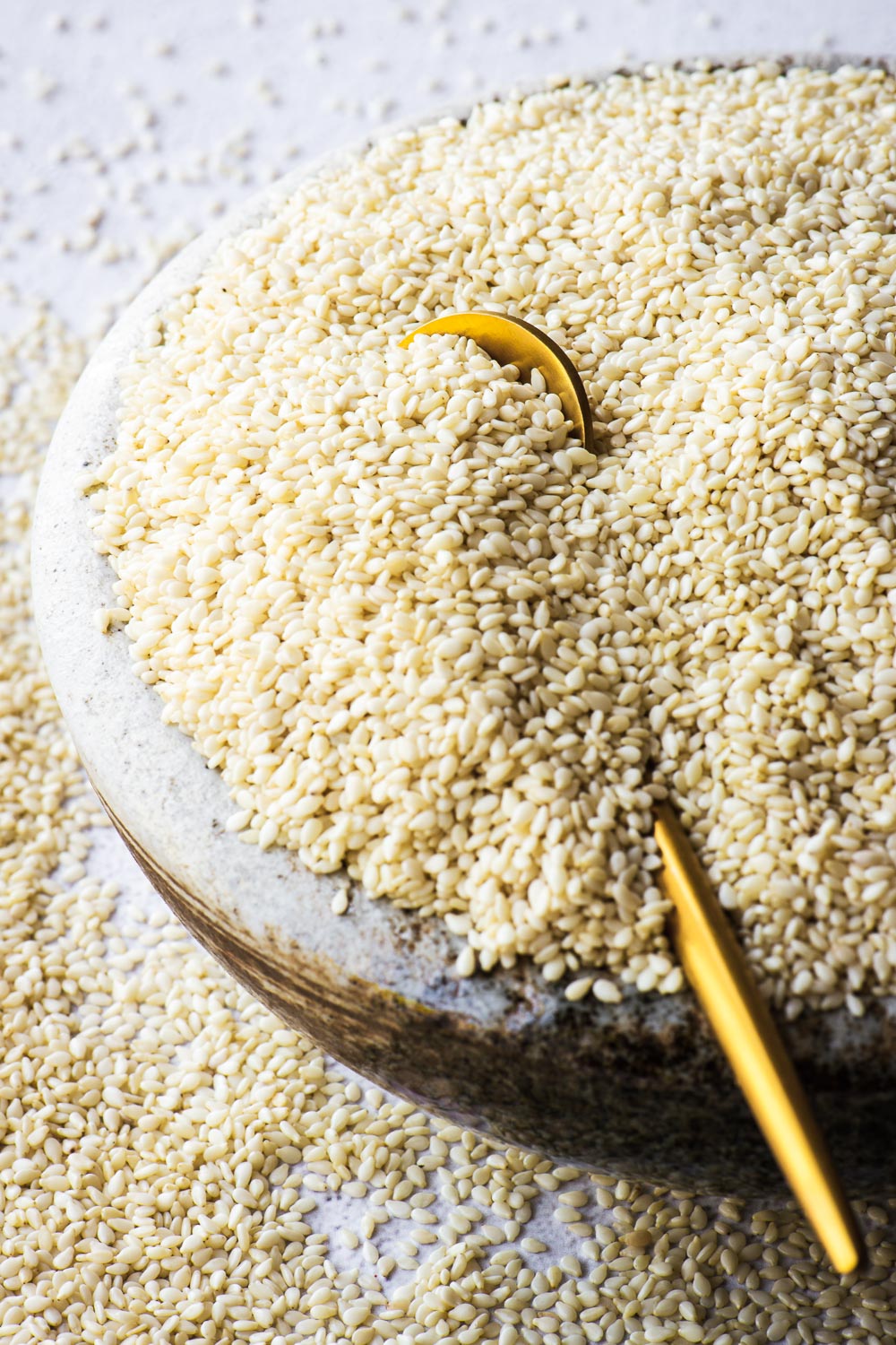 Close-up of sesame seeds in ceramic bowl with a small gold spoon.
