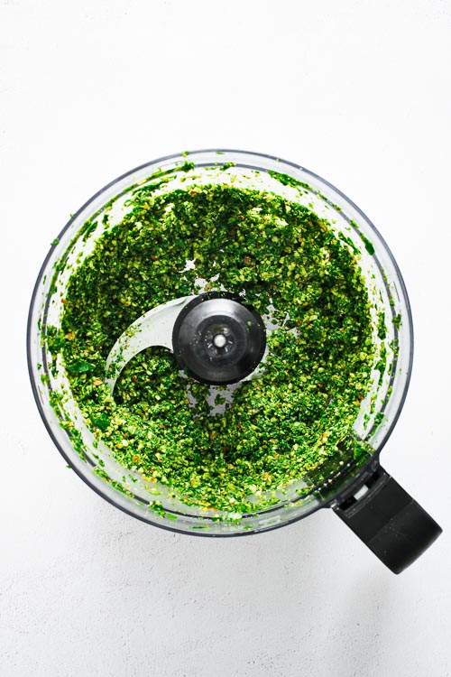 Kale, basil and almond pesto blended in a food processor and viewed from above.