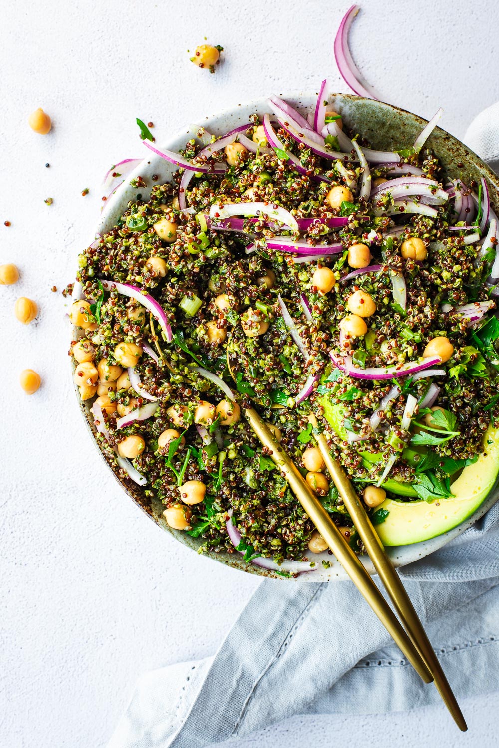 Mixed quinoa and kale pesto salad with chickpeas, red onions and avocado with chickpeas spilling over the side of the bowl.