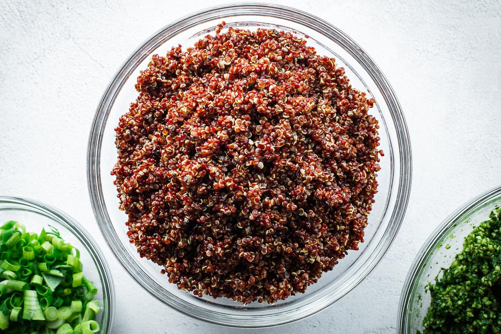 Perfectly cooked red quinoa in a glass bowl on a light concrete surface.