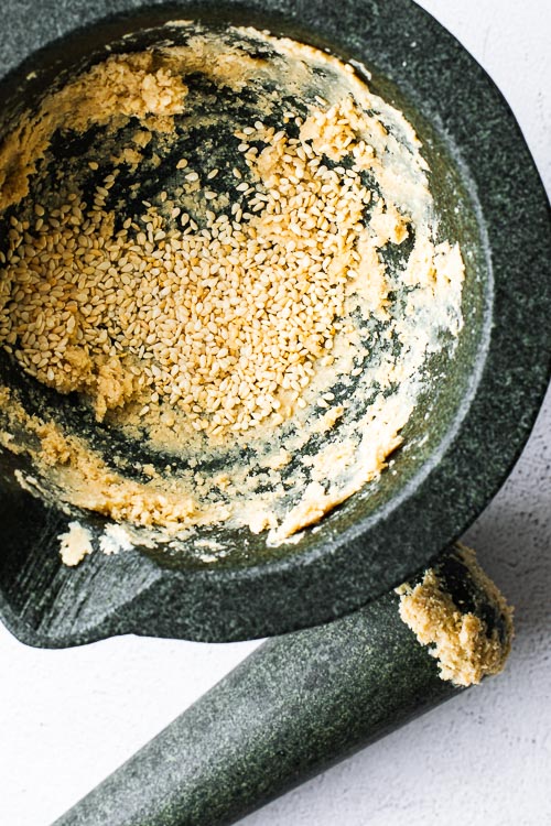 Sesame seeds in a mortar with pestle on the side.
