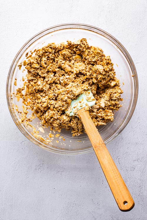 Tahini orange granola ingredients mixed in a glass bowl with a spatula.