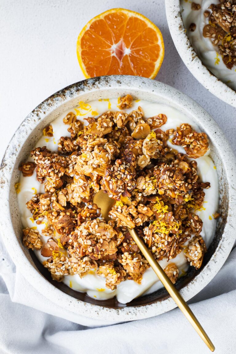 Tahini granola with sesame seeds, almonds, orange zest and honey, served on thick yoghurt in a ceramic bowl.