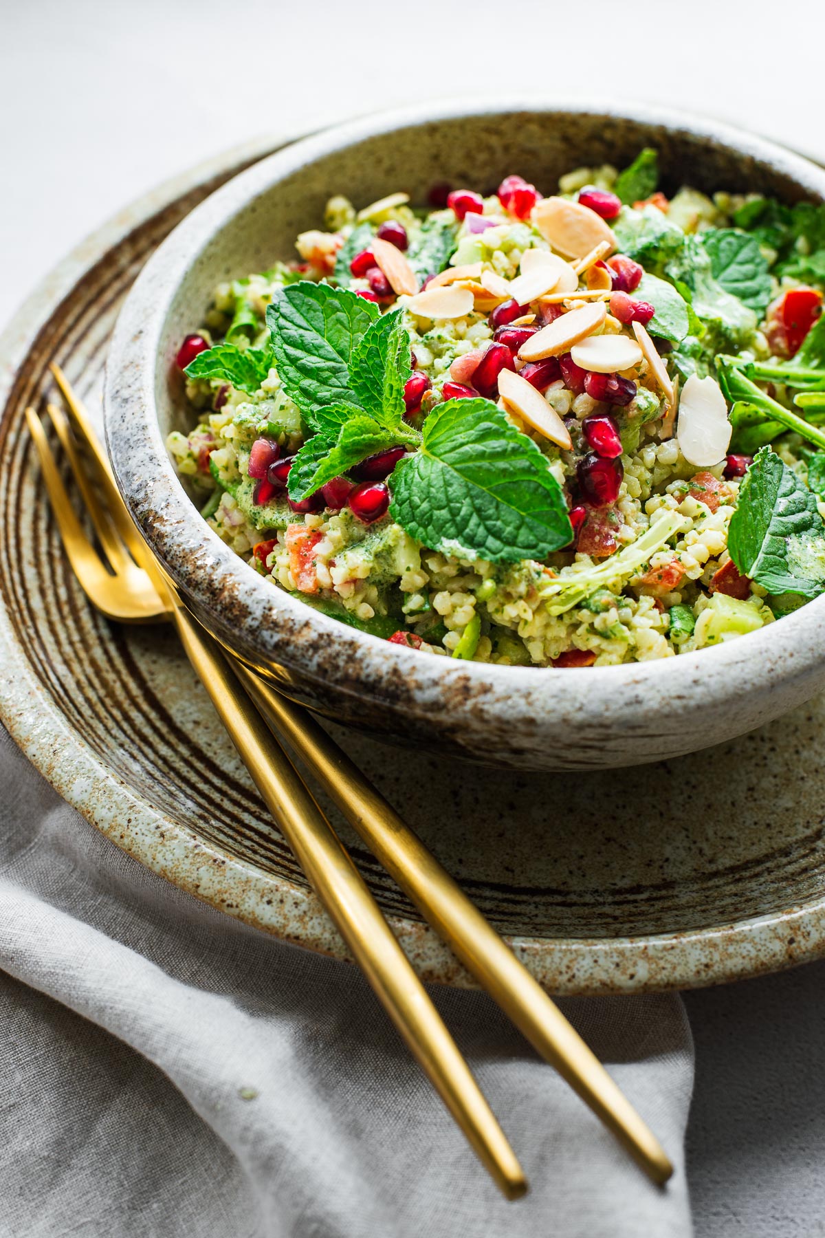 A portion of bulgur wheat salad with tahini herb dressing in a ceramic bowl with gold cutlery.