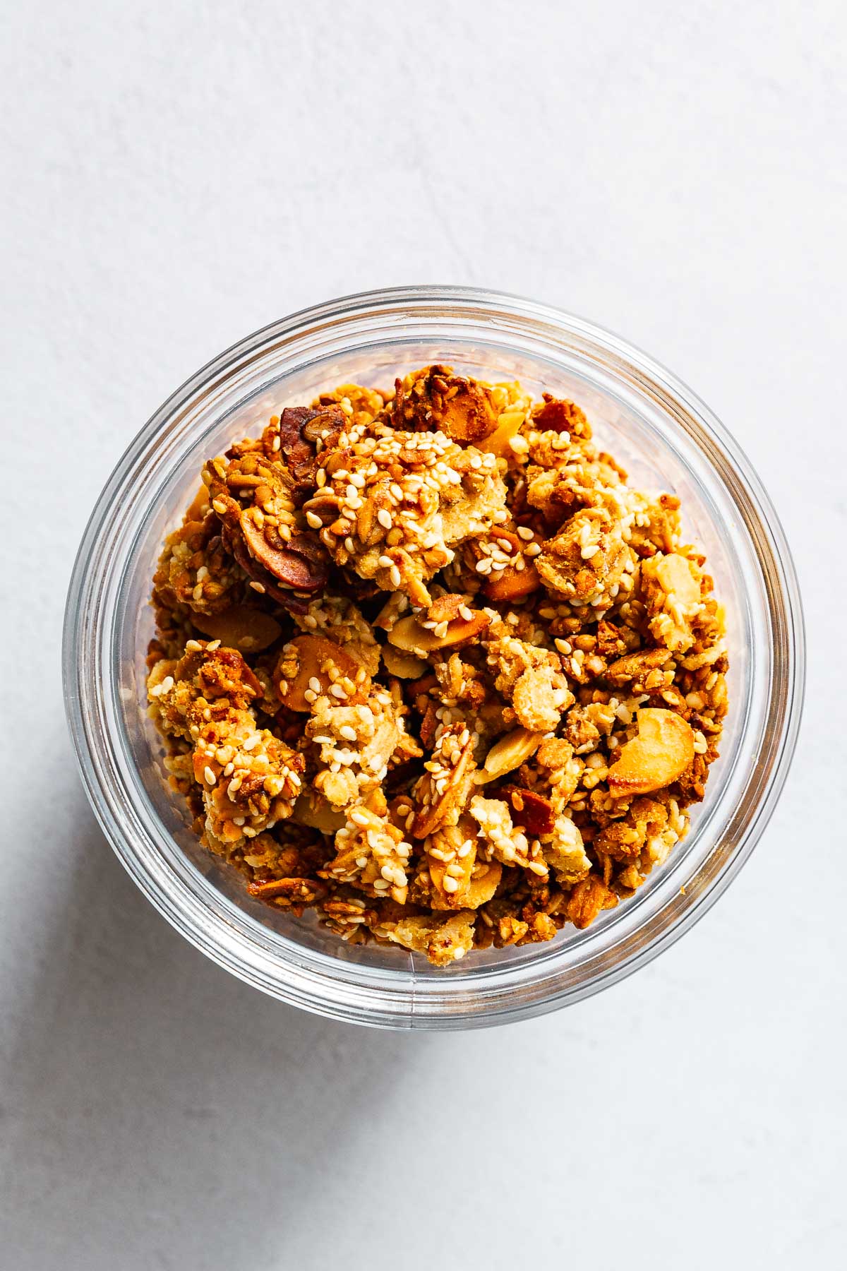 Chunky tahini orange granola with sesame seeds and flaked almonds in glass jar.