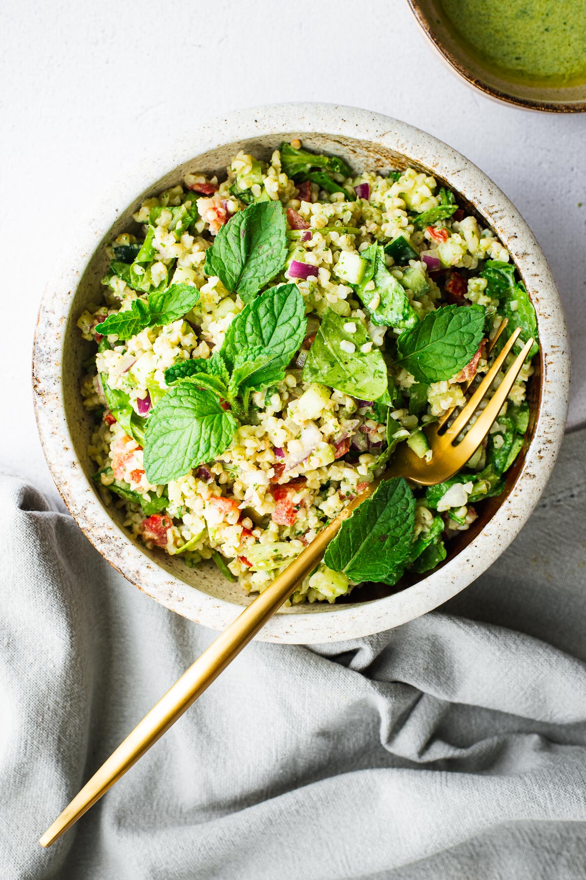 A small ceramic bowl with bulgur wheat salad with fresh mint, tahini herb dressing and Arabic chopped salad viewed from above.