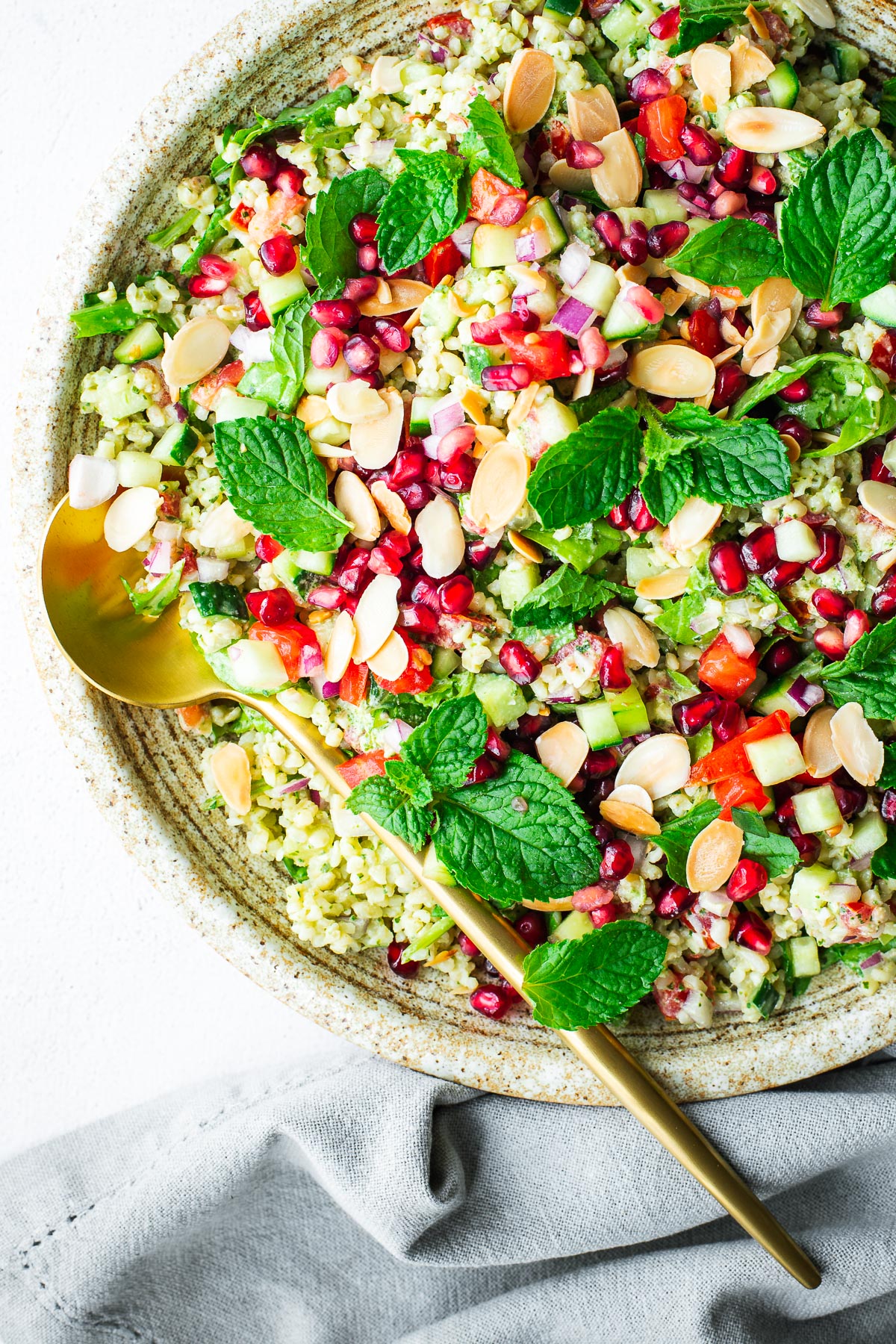 Lebanese-inspired bulgur wheat salad served as a side dish in a serving bowl with gold serving spoon and topped with mint and pomegranate.
