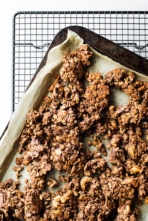 Clusters of baked vegan peanut butter granola on a parchment-lined sheet pan.