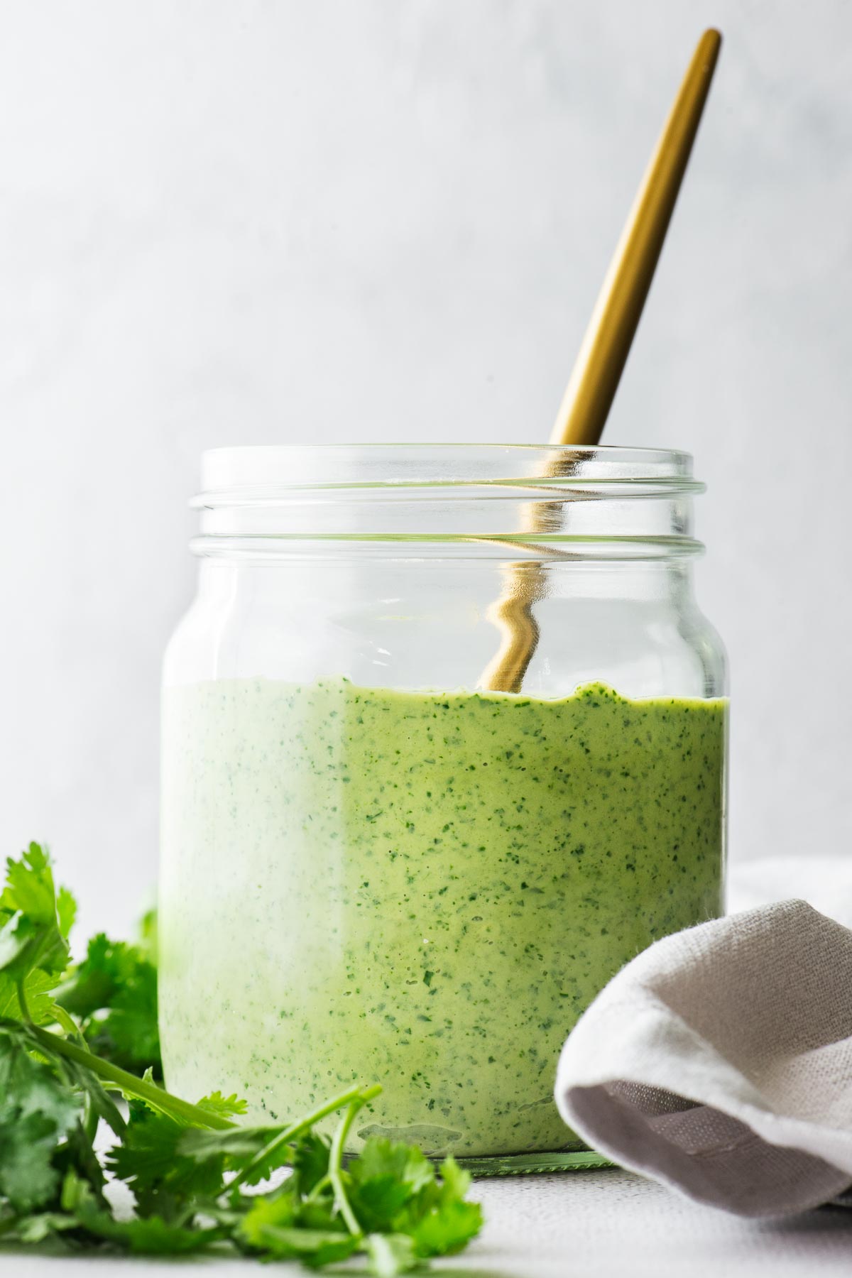 A mason jar with green tahini sauce and gold spoon viewed from a side angle.