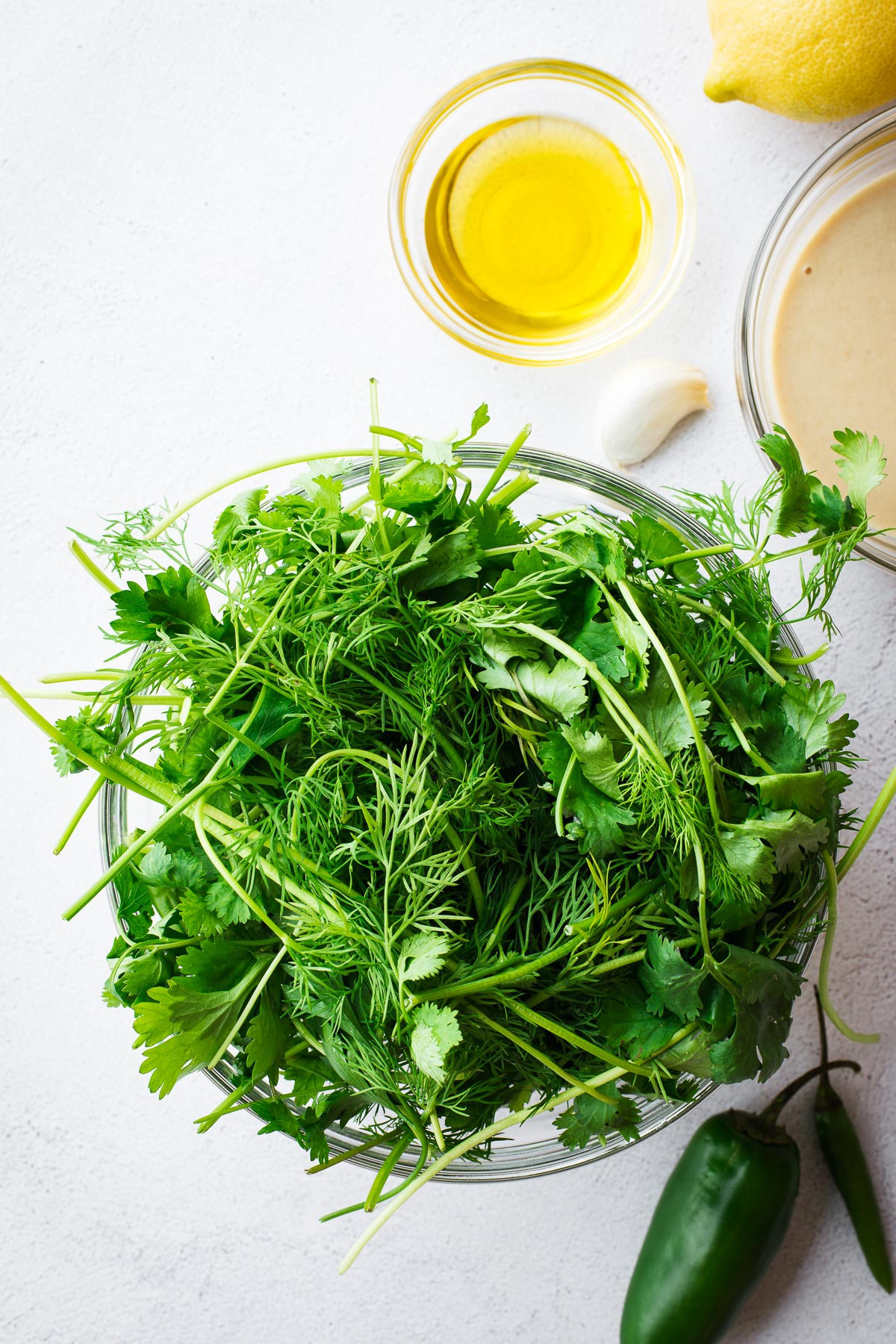 A selection of fresh herbs, including dill, flat-leaf parsley, coriander and mint, in a glass bowl surrounded by ingredients.