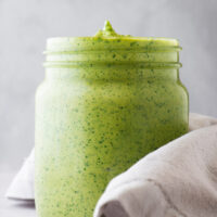 A glass jar with thick green tahini sauce.