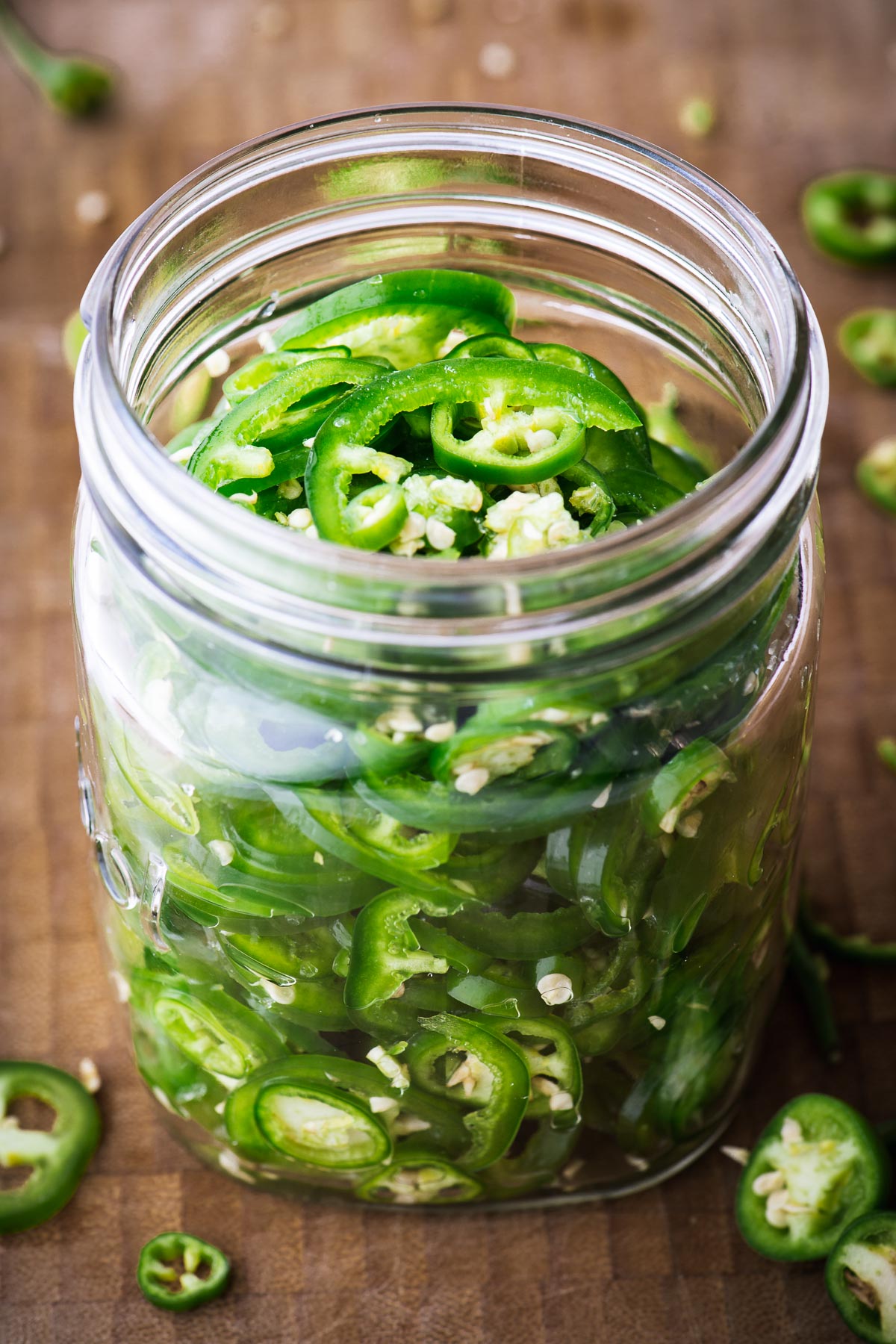 Sliced green chillies in a mason jar on a bamboo chopping board with an open lid.