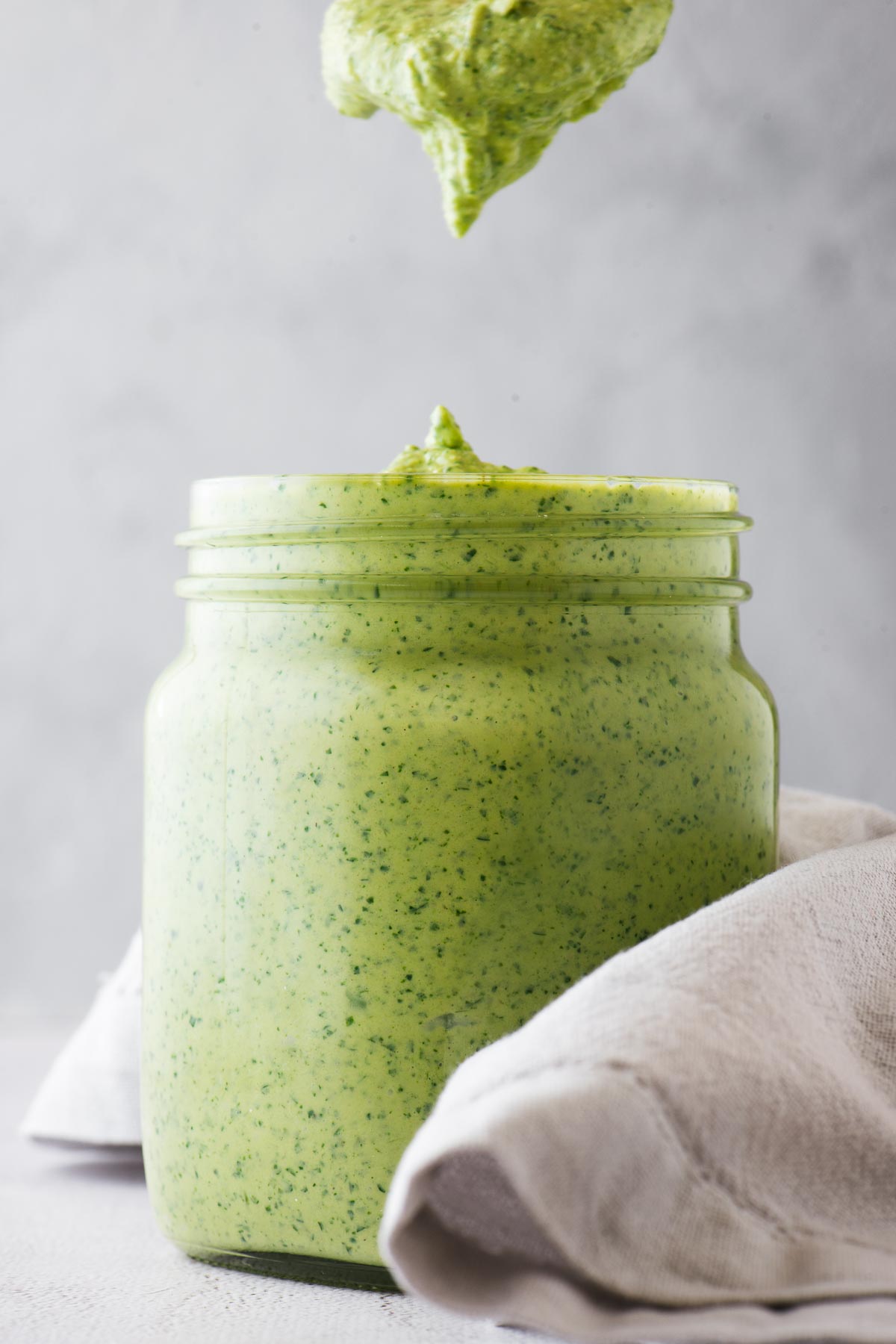 A mason jar filled to the brim with thick vegan green tahini sauce.