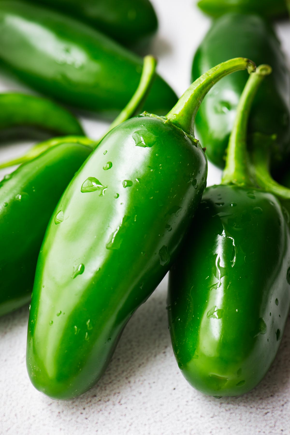 A close-up view of green jalapeño chillies with water droplets.