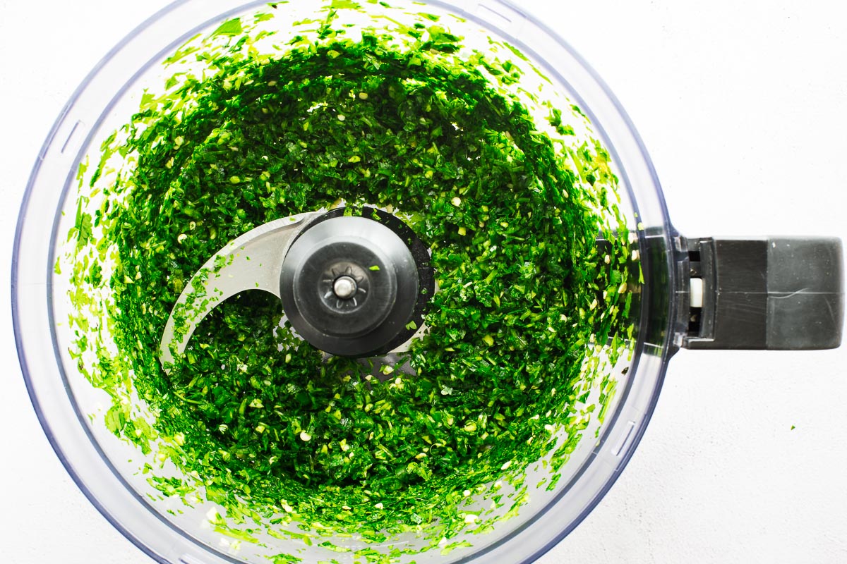 Chopped herbs in a food processor viewed from above.