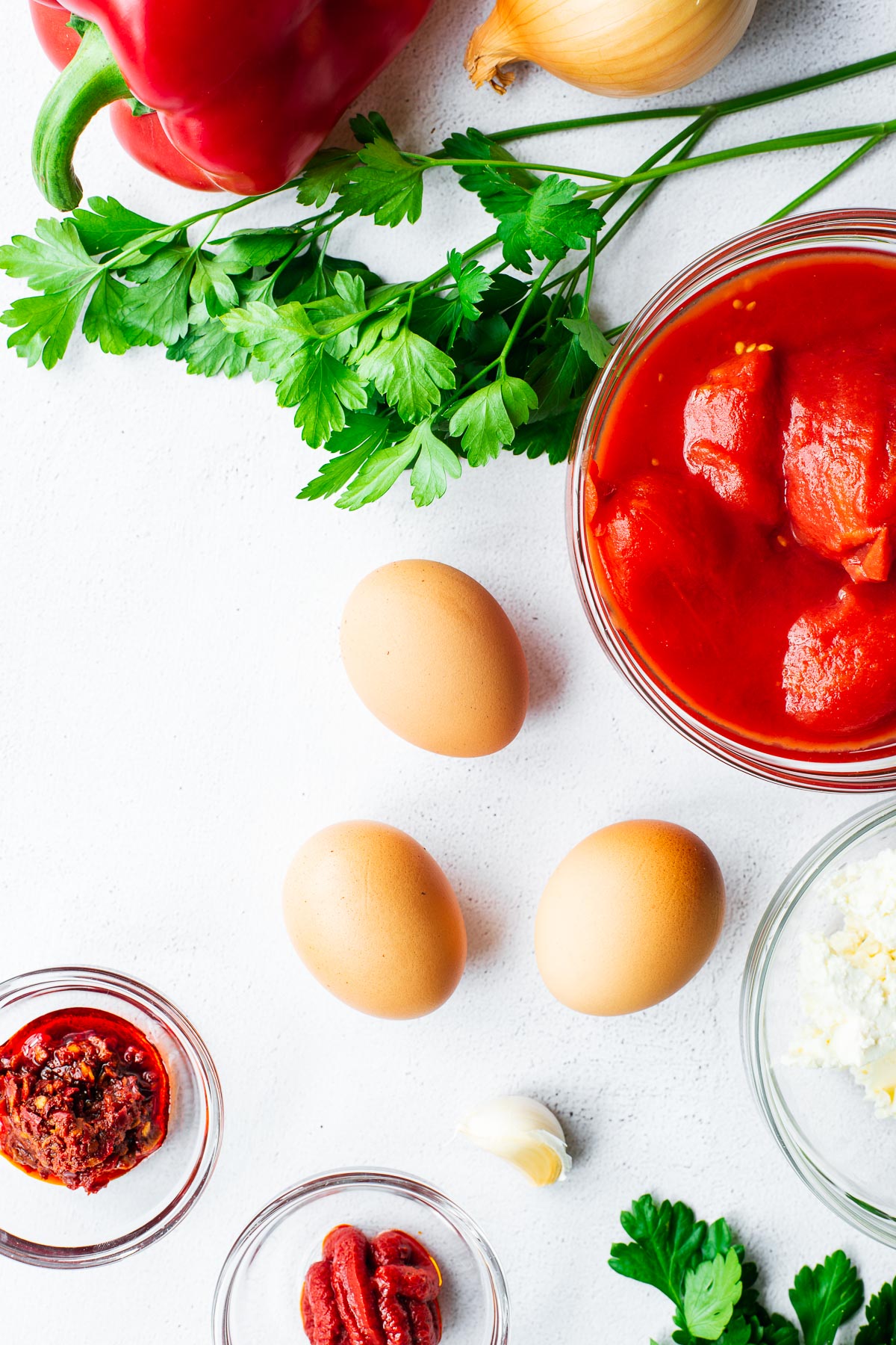 Whole eggs and shakshuka sauce ingredients arranged in a flatlay.