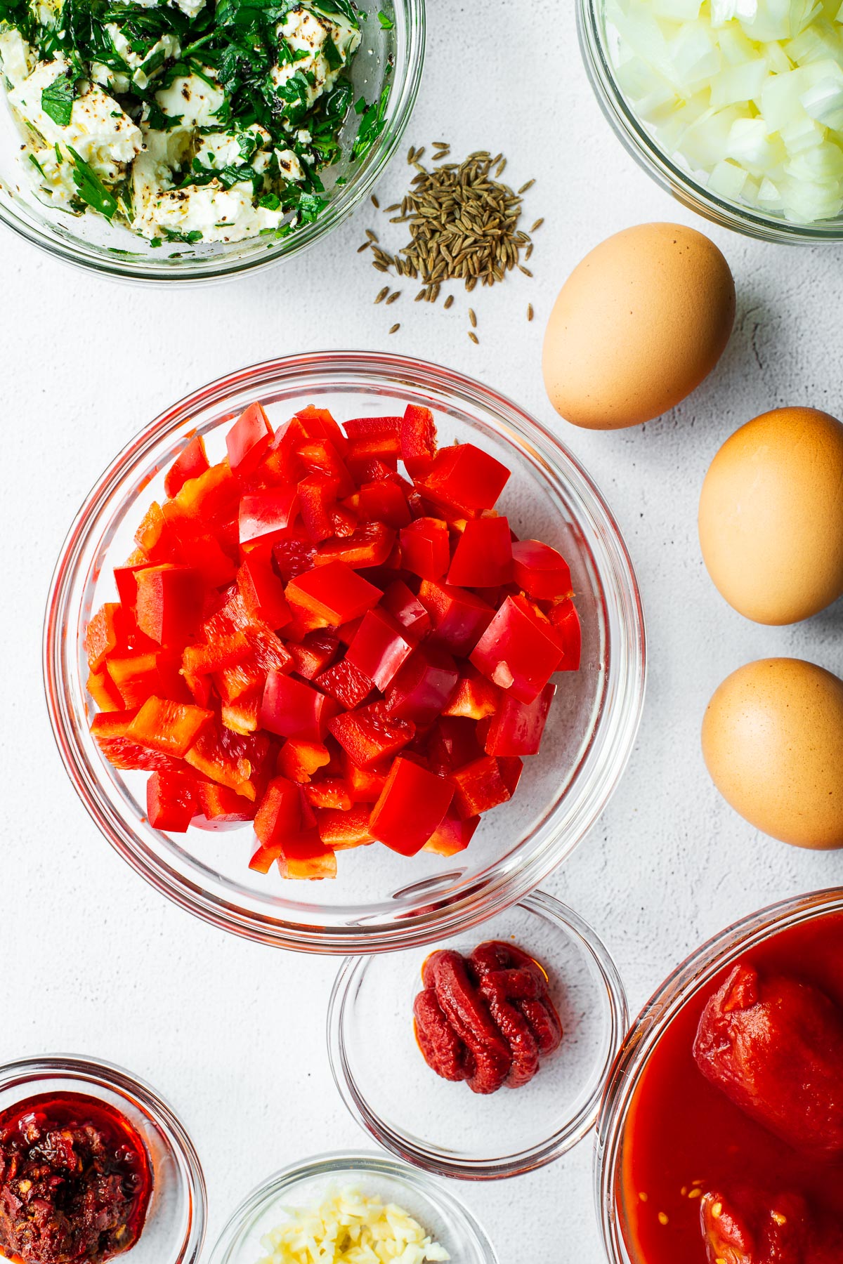 Prepared ingredients for shakshuka with feta in glass bowls viewed from above.