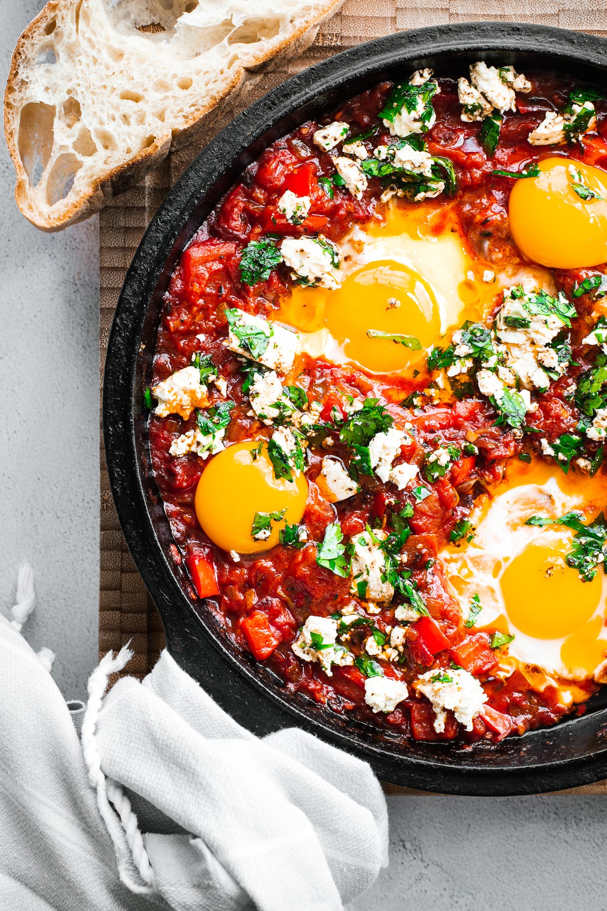 Harissa shakshuka with whole eggs and egg yolk and feta in a cast iron skillet viewed from above.