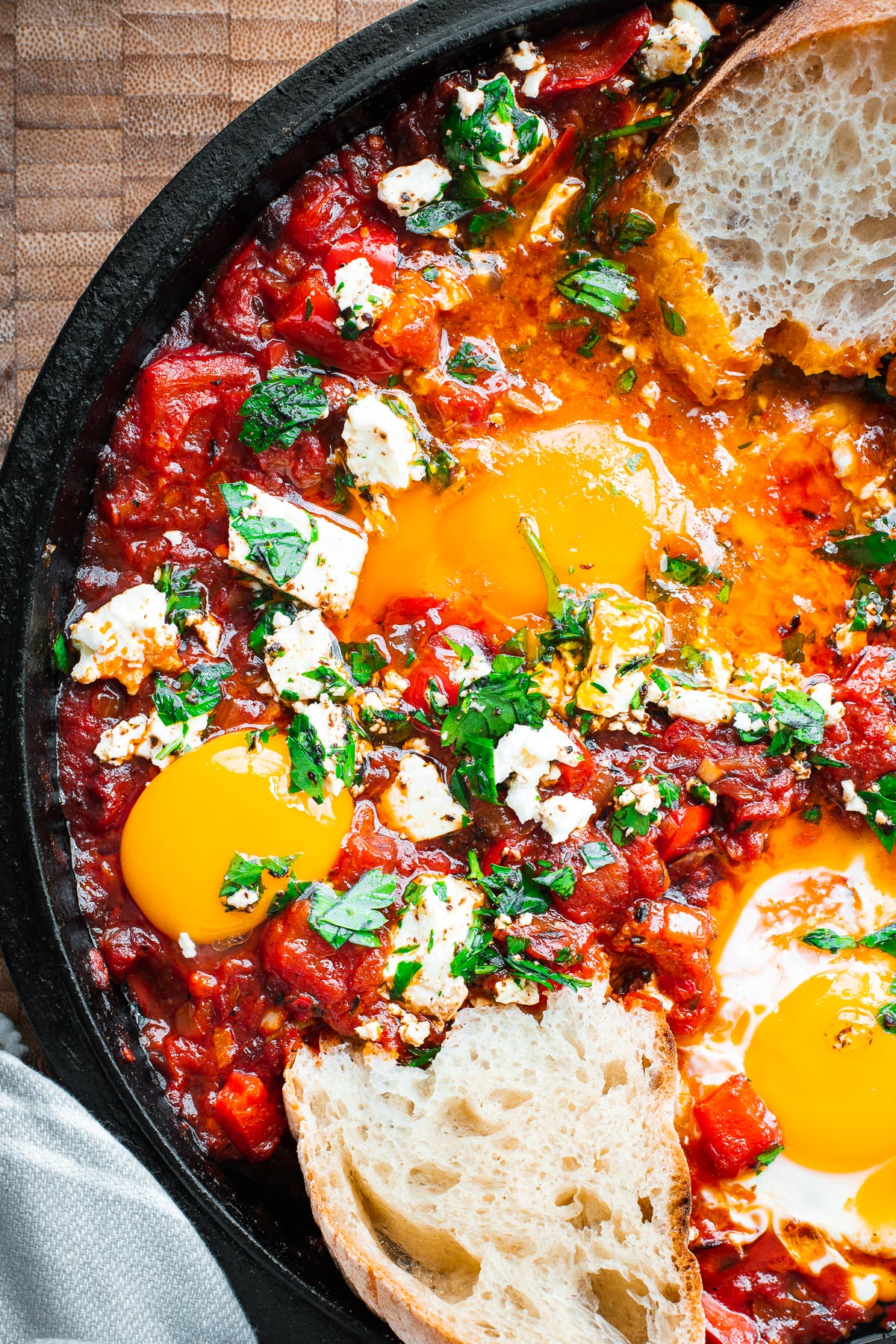 Harissa shakshuka with bread dipped into a very runny egg yolk in a cast iron skillet.