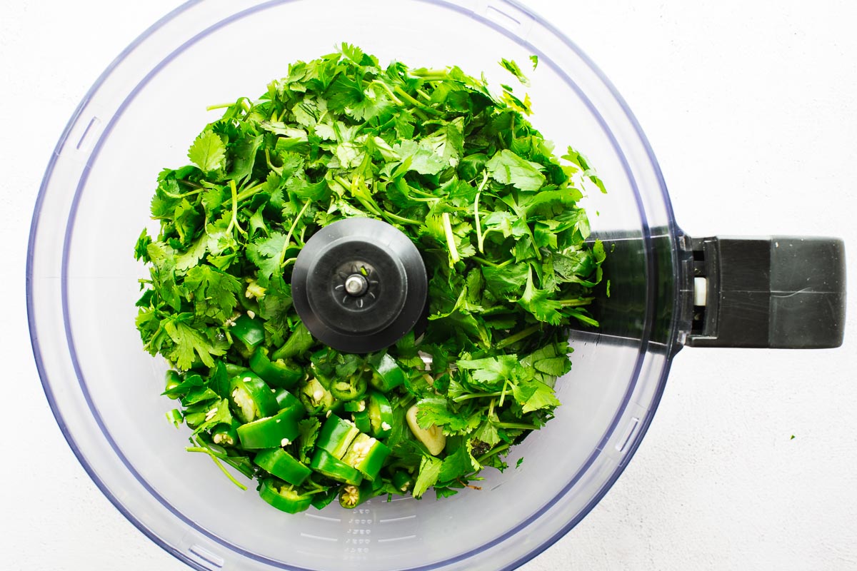Coriander leaves and green chillies in a food processor viewed from above.