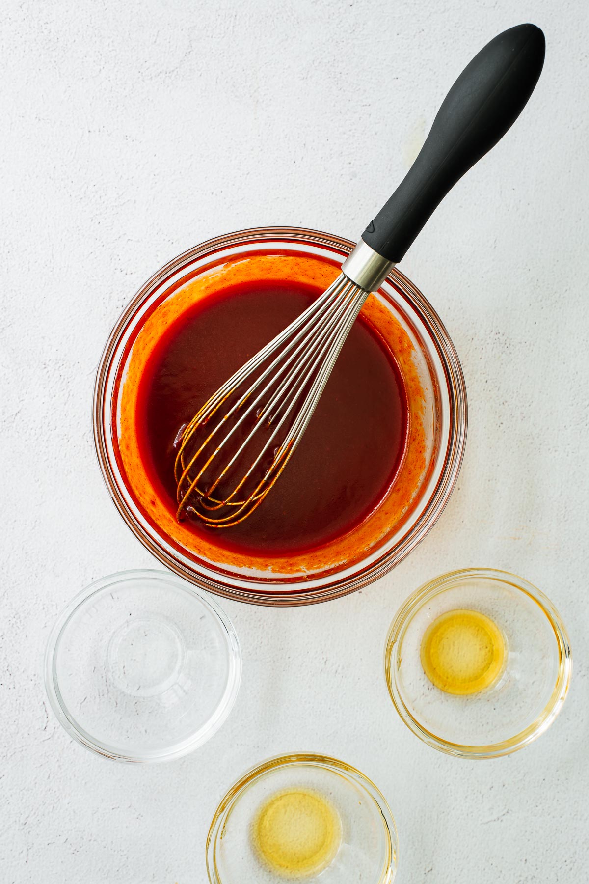 Top down view of empty glass bowls and bibimbap sauce ingredients whisked together in a glass bowl.