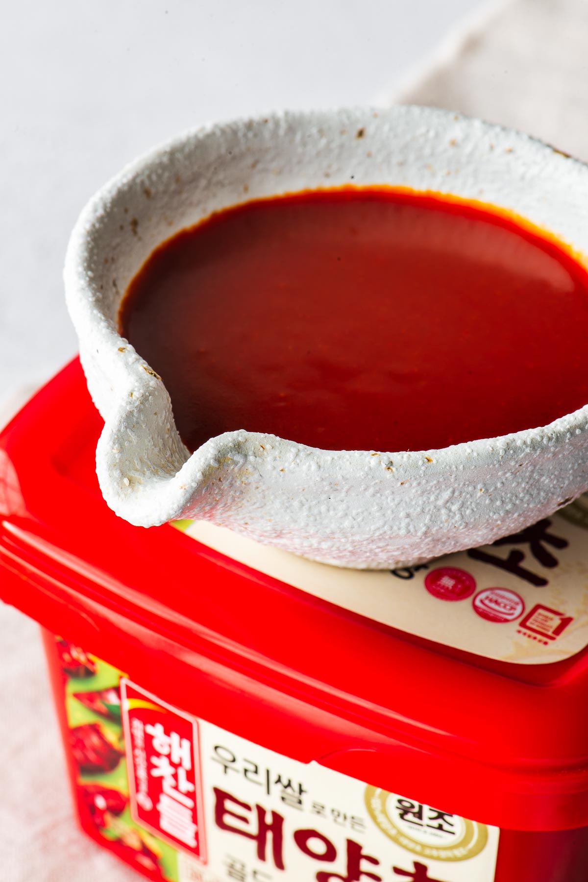 Close-up of bibimbap sauce in a white ceramic cup on top of a tub of gochujang paste.
