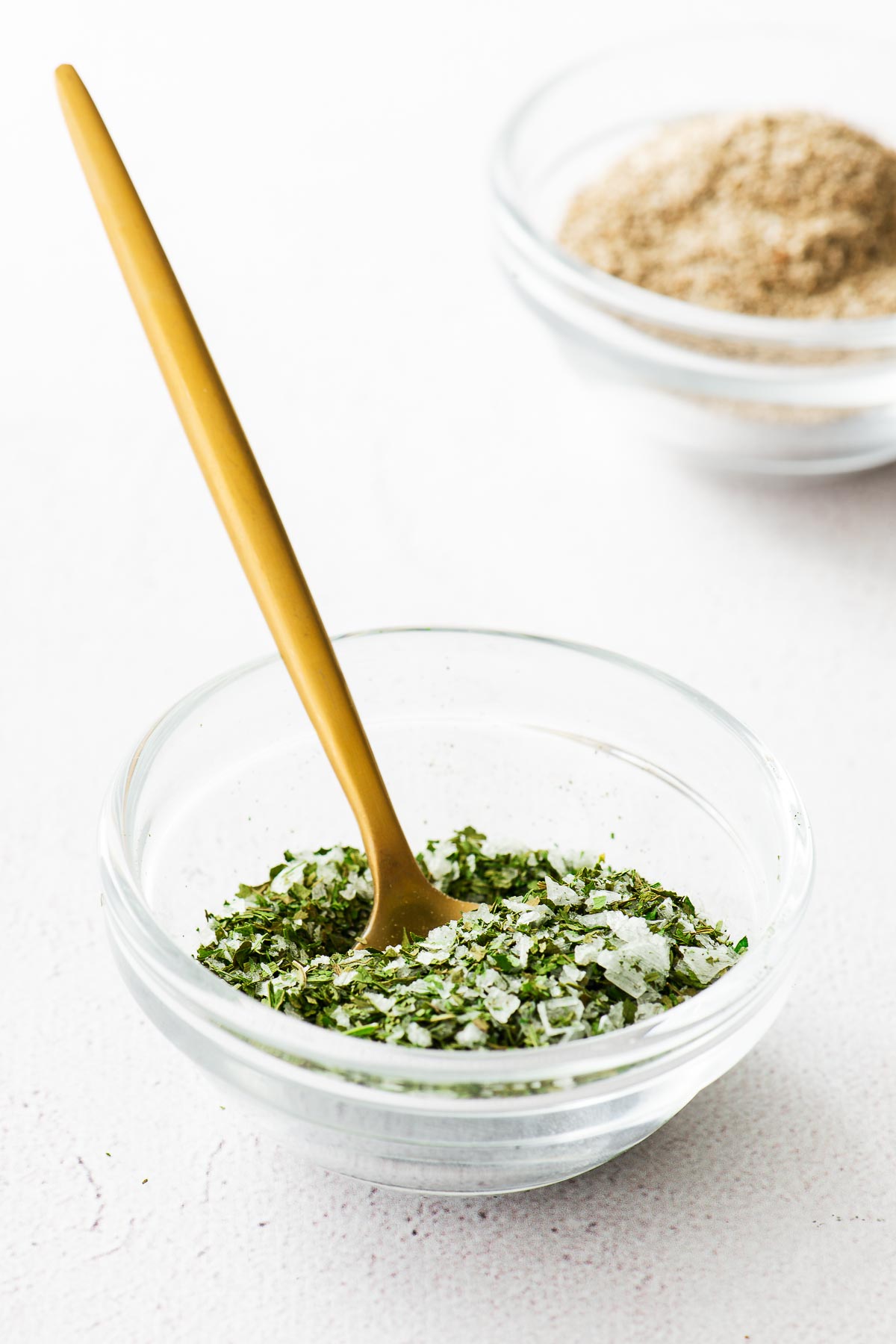 Celery salt substitute made from dehydrated celery leaves and salt in a glass bowl with a golden spoon.