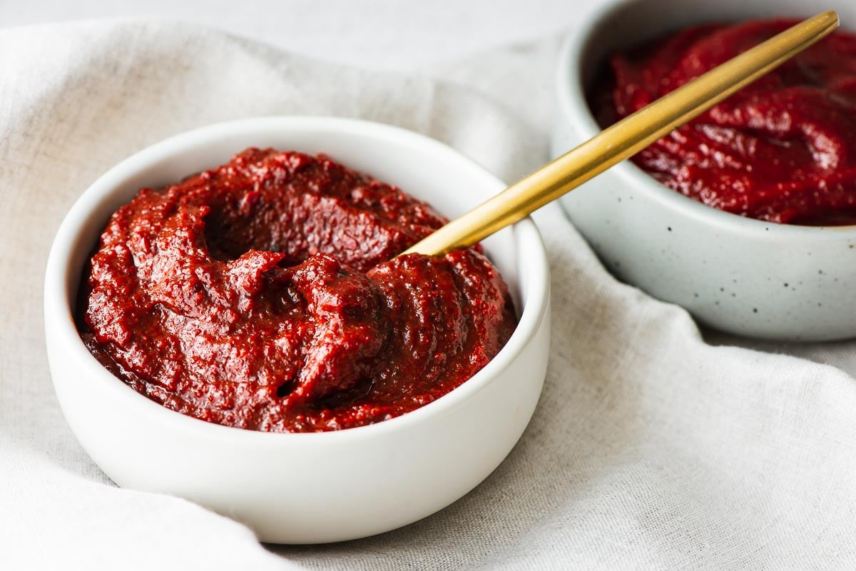 A bowl of homemade gochujang substitute with a gold spoon and real gochujang in the background.