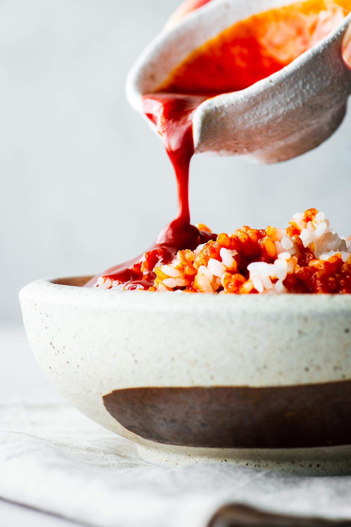 Pouring gochujang sauce from a white pourer onto a bowl of rice.
