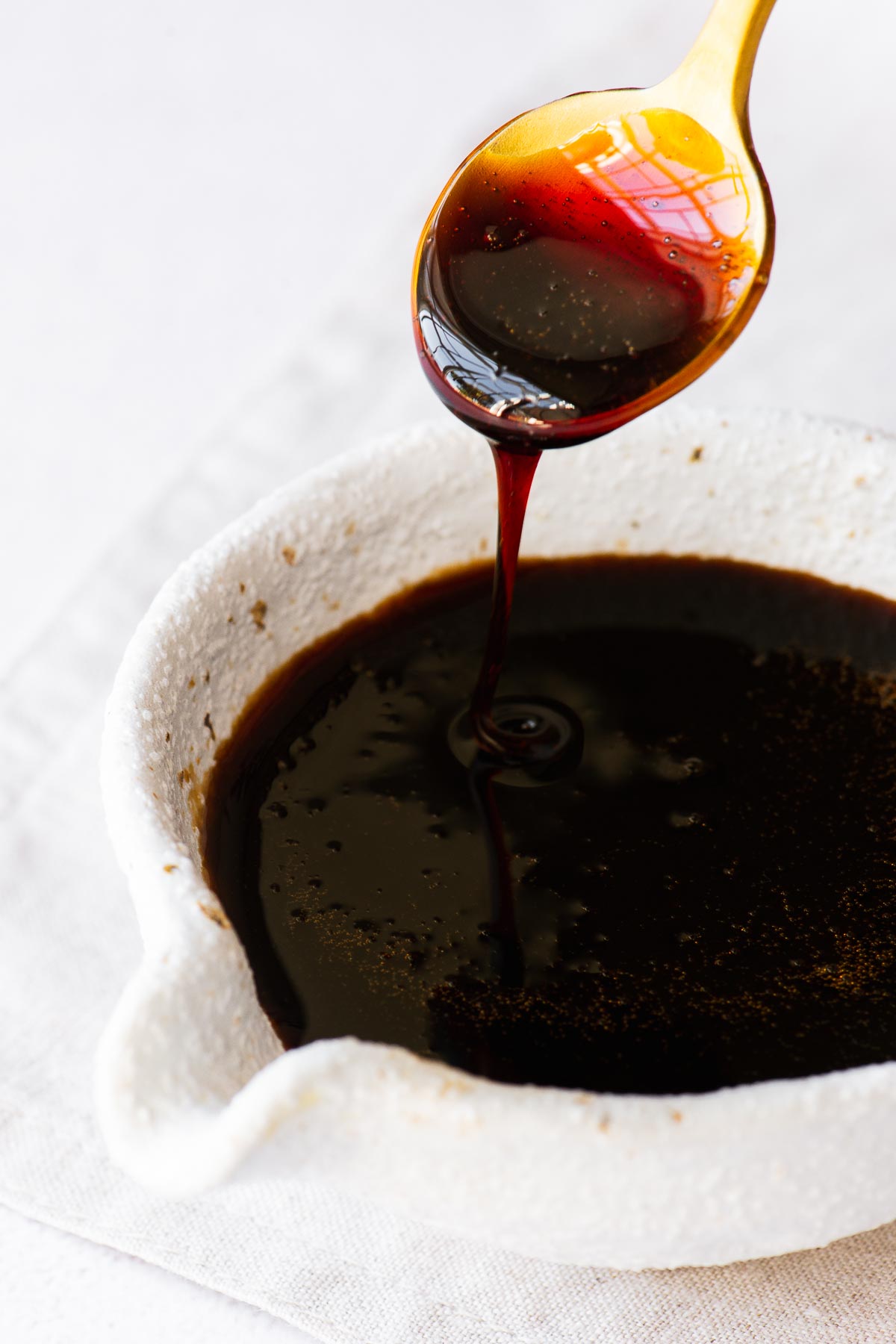 Homemade sweet soy sauce substitute (Indonesian kecap manis) drizzling from a teaspoon into a soy sauce pourer.