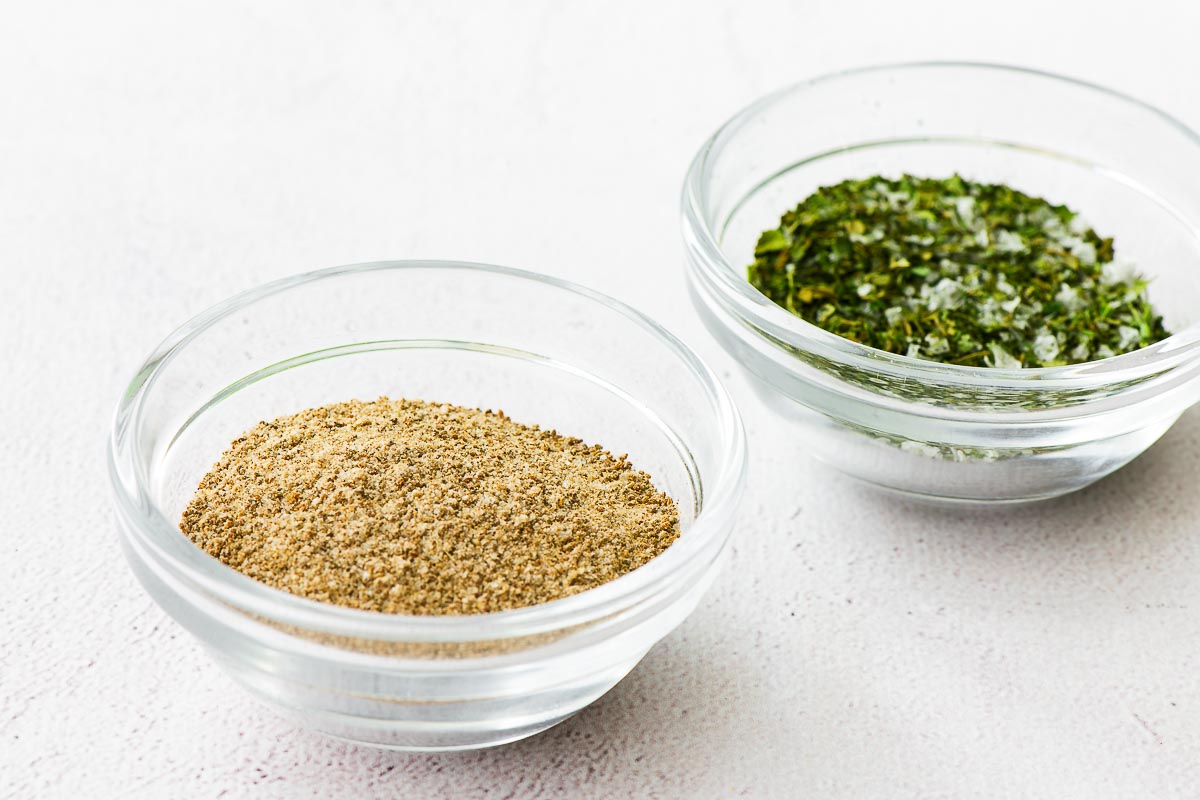 Two types of homemade celery salt, one made from celery seeds and one from dried celery leaves, in small glass bowls.