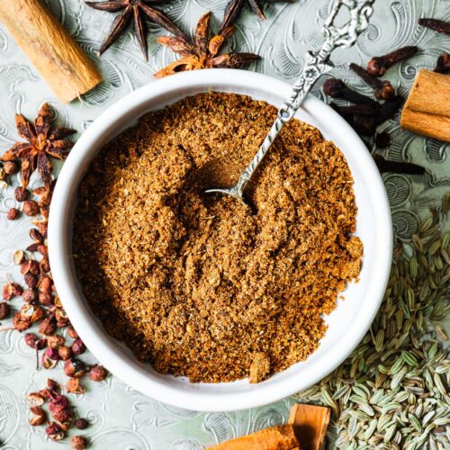 Homemade Chinese five-spice substitute with Chinese cinnamon, star anise pods, fennel seeds, Sichuan peppercorns and cloves. The five-spice powder is in a small bowl surrounded by spices.