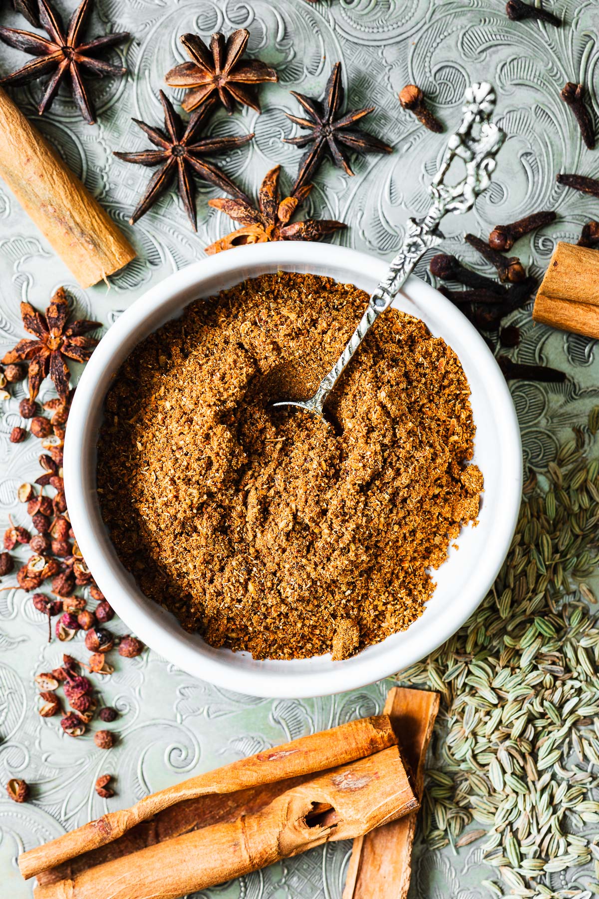 Homemade Chinese five-spice substitute with Chinese cinnamon, star anise pods, fennel seeds, Sichuan peppercorns and cloves. The five-spice powder is in a small bowl surrounded by spices.