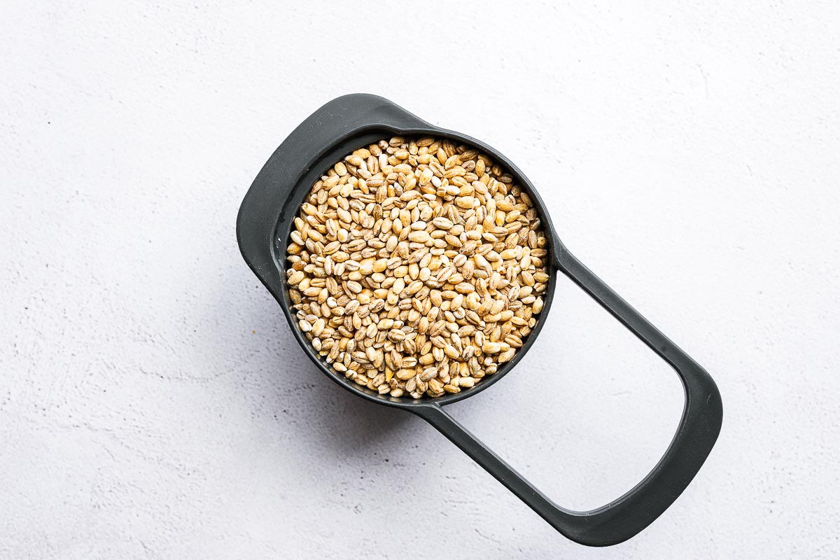 A cup of uncooked pearl barley on a light concrete background viewed from above.