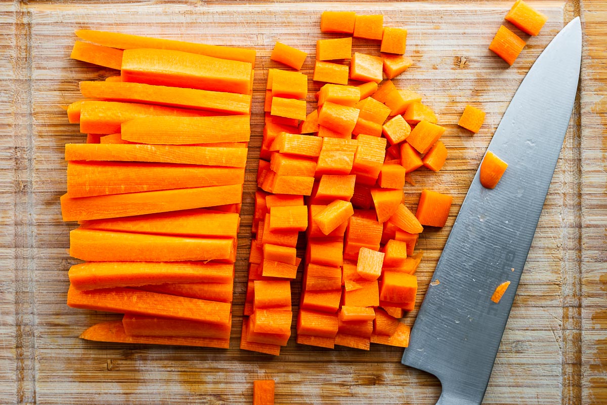 Dicing carrots that are sliced into batons on a bamboo chopping board.
