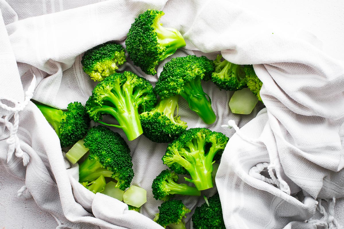 Drying cold, blanched broccoli florets with a kitchen towel.