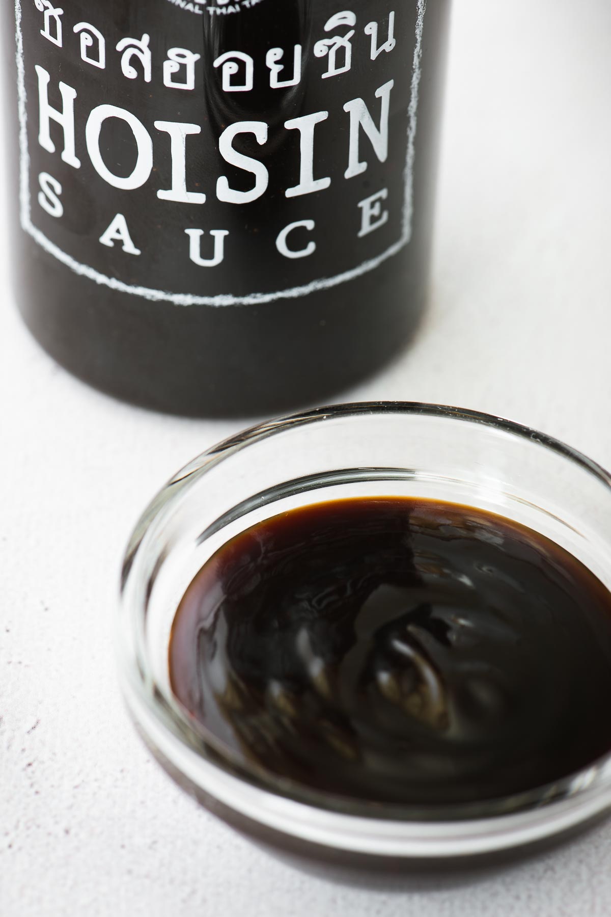 Hoisin sauce in a small glass bowl with a labelled hoisin sauce bottle in the background.