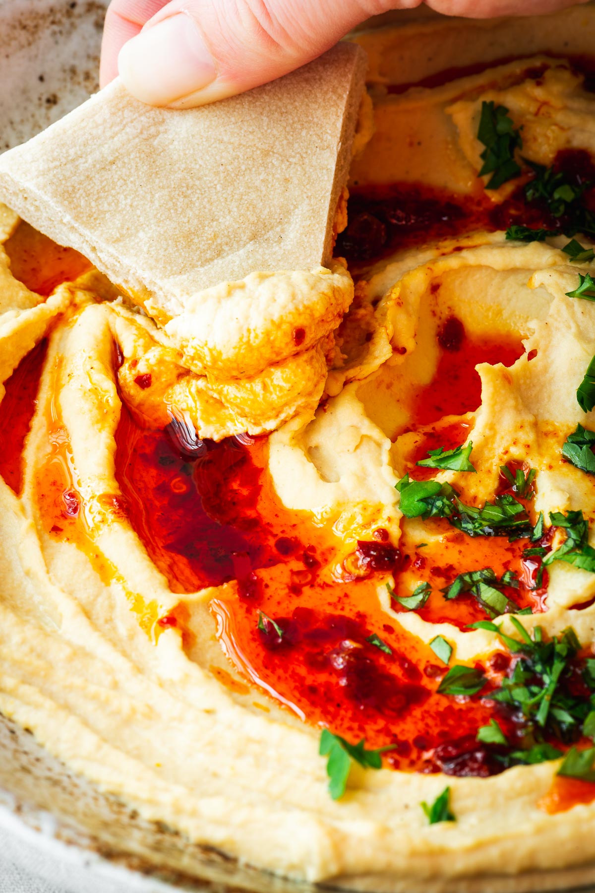 Close-up of smooth hummus without garlic with a hand scooping hummus with a pita triangle.