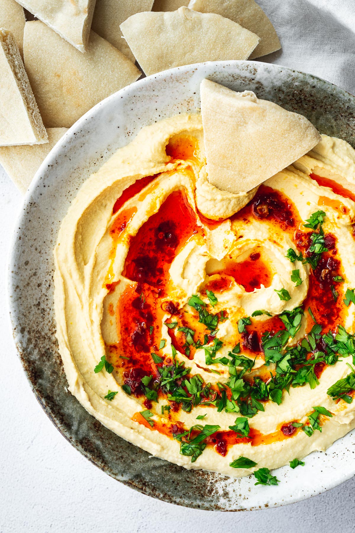 Top down view of a bowl of hummus with pita triangles.